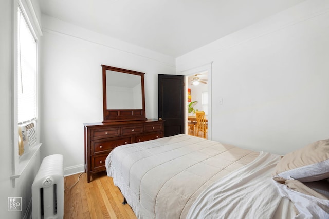 bedroom featuring radiator heating unit, light wood-style floors, and baseboards