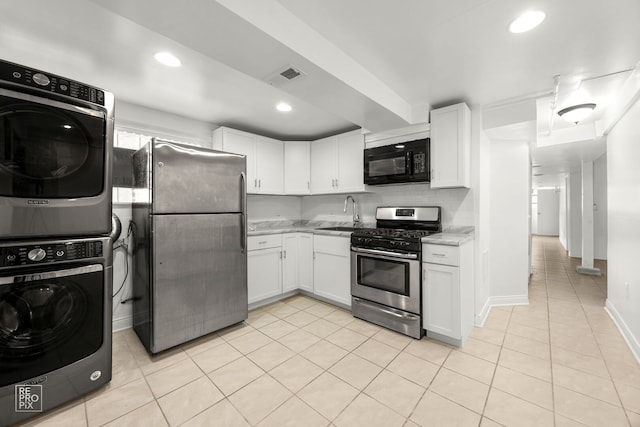 kitchen with appliances with stainless steel finishes, estacked washer and dryer, a sink, white cabinetry, and light tile patterned floors