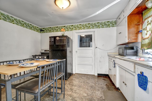 kitchen with black appliances, white cabinets, light countertops, stone finish floors, and a sink