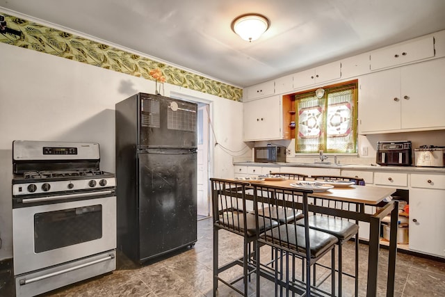 kitchen featuring stainless steel range with gas cooktop, freestanding refrigerator, and white cabinets