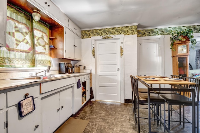 kitchen featuring white cabinetry, light countertops, a sink, stone finish flooring, and crown molding