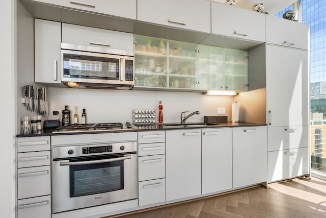 kitchen with stainless steel appliances, a sink, dark countertops, and white cabinets