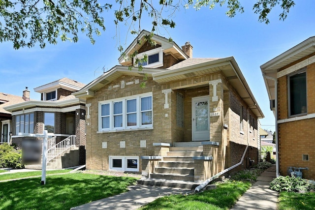 view of front of house with a chimney, a front yard, brick siding, and stairs
