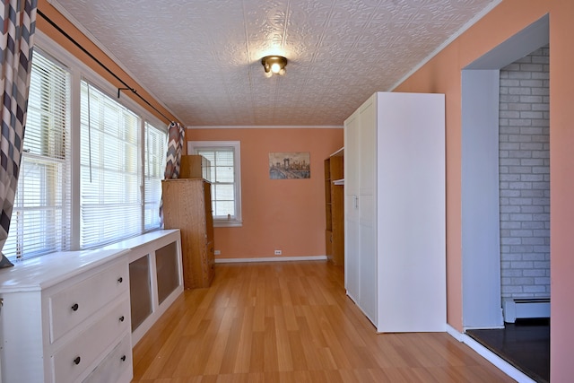 corridor featuring light wood-style floors, a baseboard radiator, baseboards, and ornamental molding