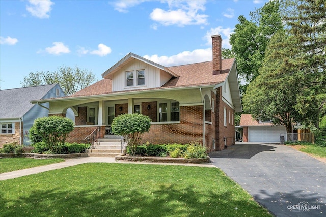 view of front facade with a porch, a chimney, an outdoor structure, brick siding, and a front yard