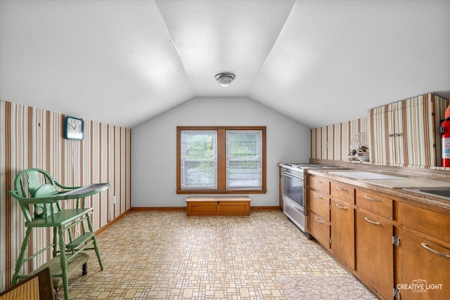 kitchen featuring stainless steel range oven, wallpapered walls, baseboards, brown cabinets, and vaulted ceiling