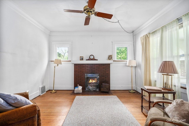 living room with plenty of natural light, ornamental molding, a ceiling fan, a brick fireplace, and baseboards