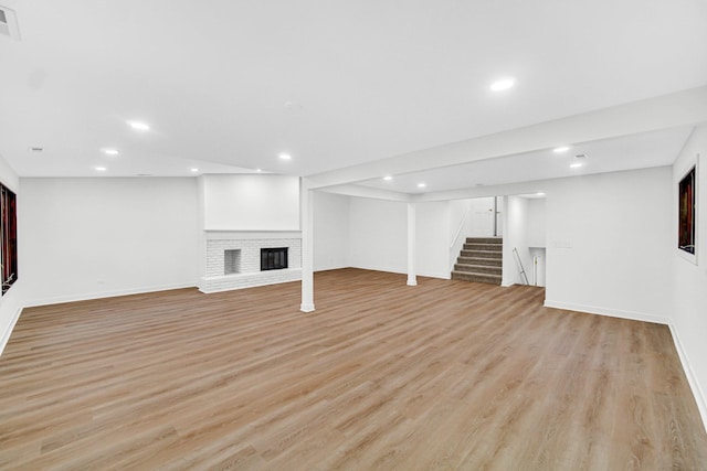 finished below grade area with stairway, light wood-style floors, baseboards, recessed lighting, and a fireplace
