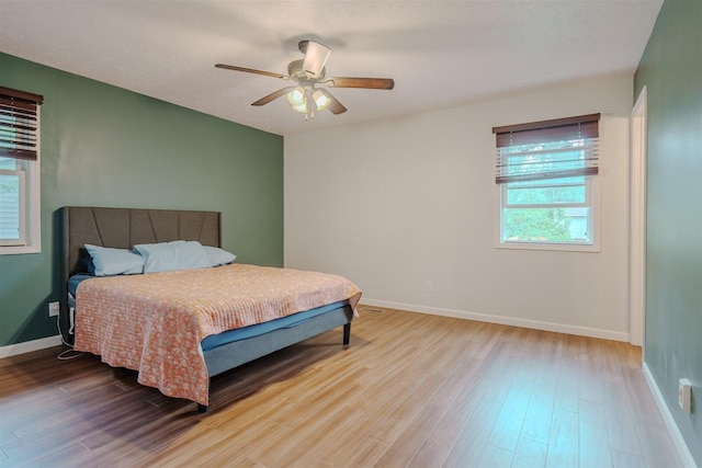 bedroom with multiple windows, wood finished floors, baseboards, and a ceiling fan