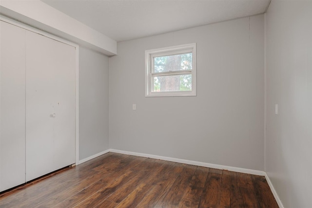unfurnished bedroom with dark wood-style flooring, baseboards, and a closet