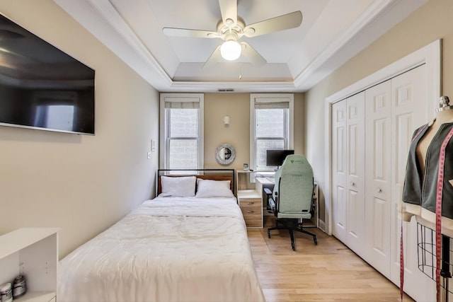 bedroom featuring a raised ceiling, light wood-type flooring, a closet, ceiling fan, and a desk