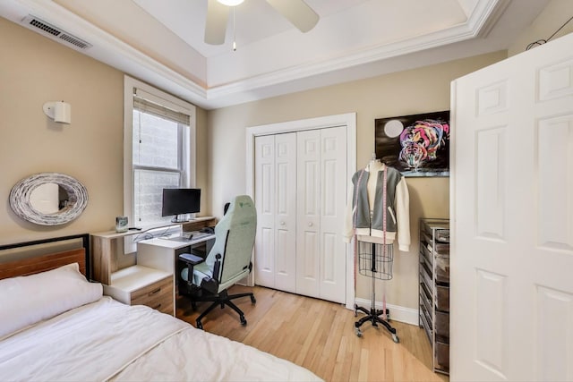 bedroom with wood finished floors, a tray ceiling, a closet, a ceiling fan, and baseboards