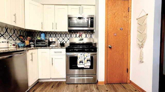 kitchen featuring appliances with stainless steel finishes, wood finished floors, stone counters, and white cabinets