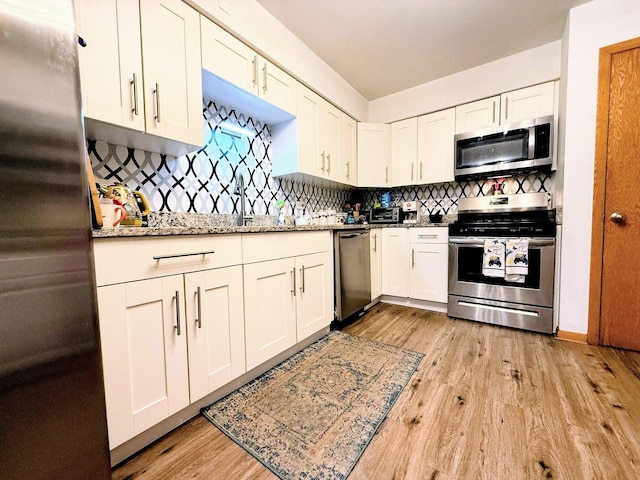 kitchen with appliances with stainless steel finishes, light wood-type flooring, backsplash, white cabinetry, and light stone countertops