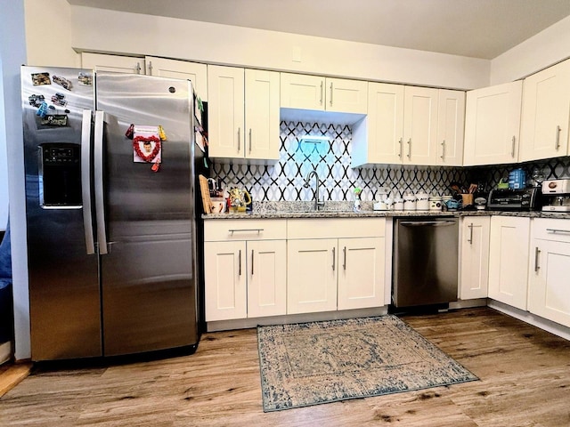 kitchen with appliances with stainless steel finishes, a sink, light wood-style floors, stone countertops, and tasteful backsplash