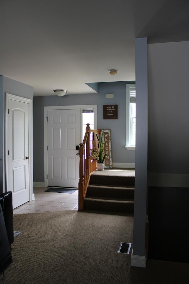 tiled foyer entrance featuring carpet flooring, stairway, and baseboards