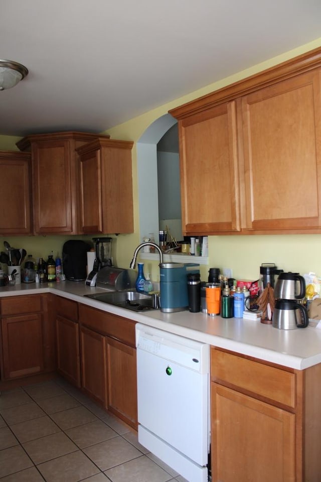 kitchen with white dishwasher, a sink, light tile patterned floors, light countertops, and arched walkways