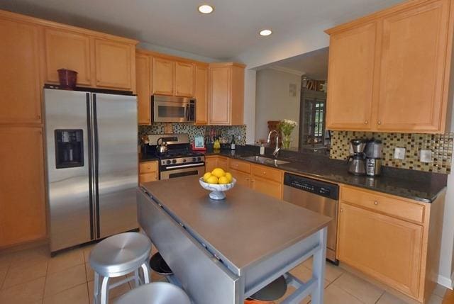 kitchen with appliances with stainless steel finishes, a sink, light tile patterned floors, dark countertops, and backsplash