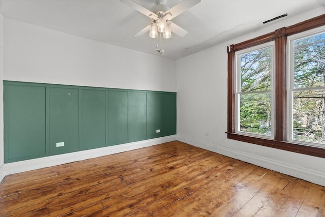 spare room featuring wood-type flooring, a wainscoted wall, ceiling fan, and a decorative wall