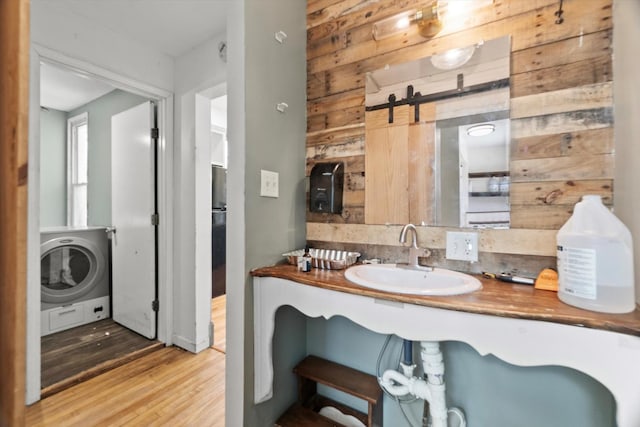 bathroom featuring a sink, washer / clothes dryer, wood finished floors, and wood walls