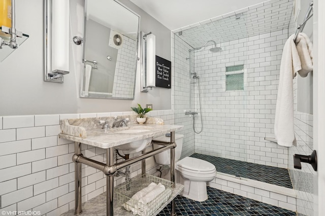 bathroom with a tile shower, tile walls, toilet, a wainscoted wall, and tile patterned flooring