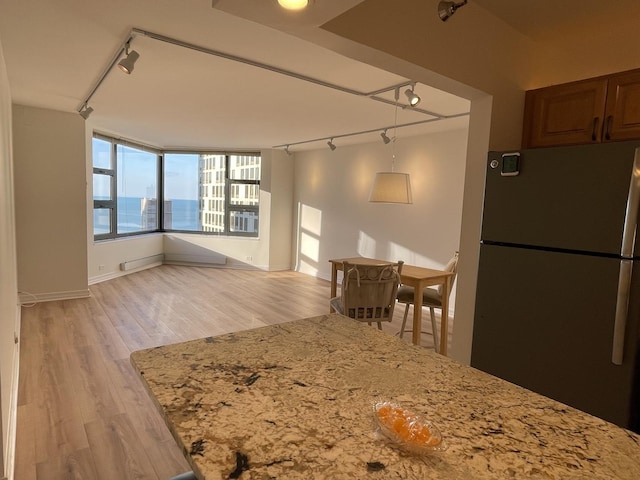 kitchen featuring freestanding refrigerator, track lighting, light wood finished floors, and light stone countertops
