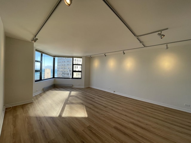 spare room with track lighting, wood finished floors, and baseboards