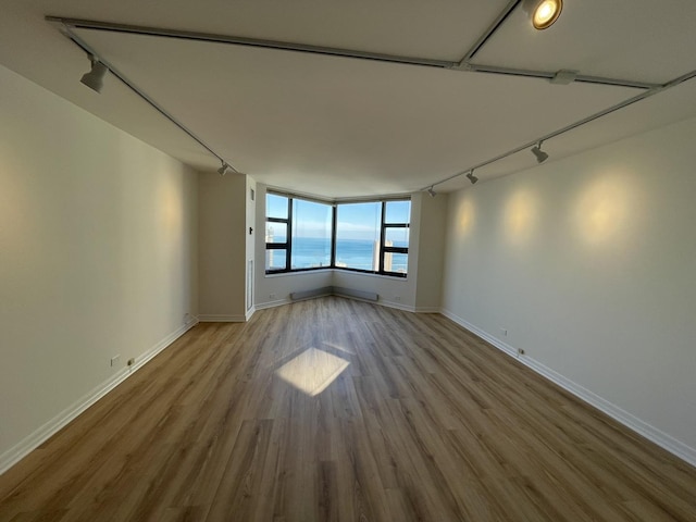 spare room featuring track lighting, wood finished floors, and baseboards