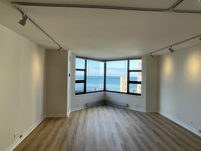 unfurnished room with track lighting, wood finished floors, baseboards, and a water view