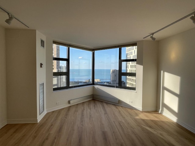 unfurnished room with rail lighting, wood finished floors, a water view, and baseboards