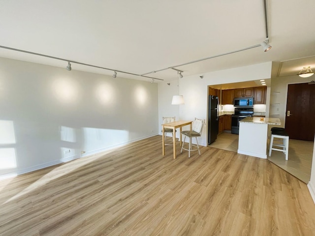 kitchen with rail lighting, black appliances, brown cabinets, and open floor plan