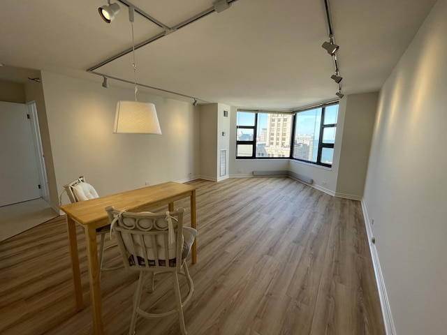 unfurnished dining area featuring rail lighting, wood finished floors, and baseboards