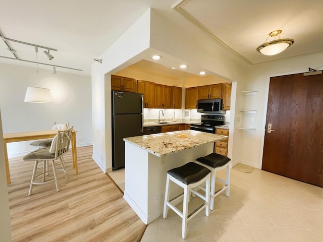 kitchen featuring black appliances, a sink, light stone countertops, brown cabinets, and a kitchen bar