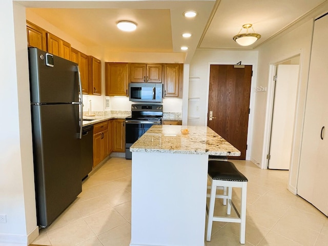 kitchen with black appliances, a center island, light stone counters, light tile patterned floors, and brown cabinets