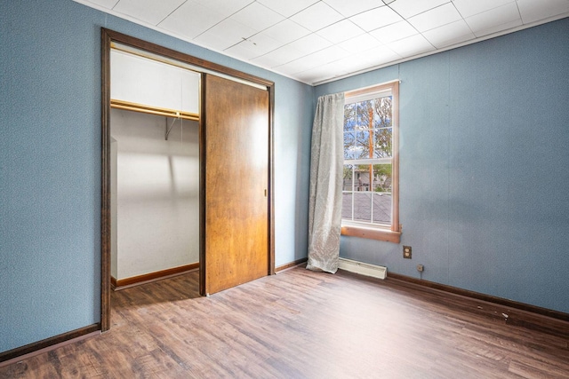unfurnished bedroom with wood finished floors, baseboard heating, a closet, and baseboards
