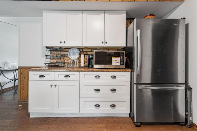 kitchen featuring appliances with stainless steel finishes, white cabinets, dark wood-style flooring, dark stone counters, and decorative backsplash