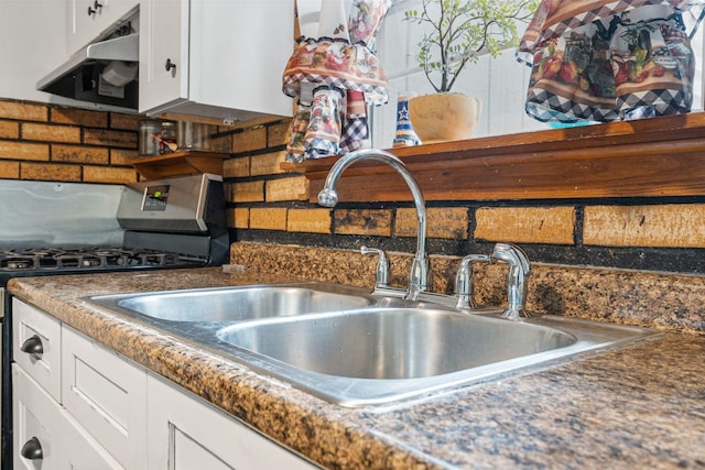 kitchen with extractor fan, stainless steel gas stove, white cabinets, backsplash, and dark countertops