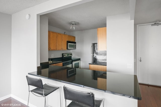 30 E Huron St Unit 2708, Chicago, IL 60611 - kitchen featuring stainless steel appliances, dark countertops, a textured ceiling, a peninsula, and brown cabinetry