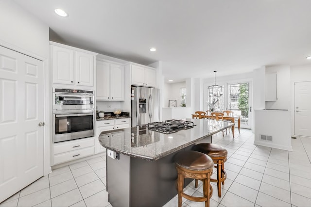kitchen with stainless steel appliances, light tile patterned floors, a kitchen bar, dark stone counters, and white cabinetry