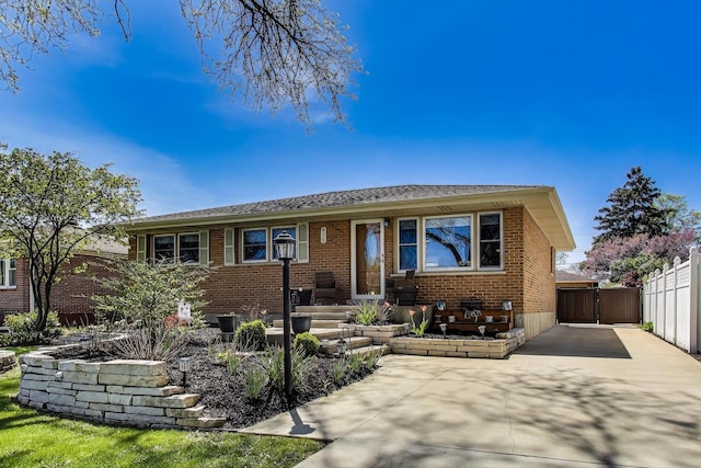 bungalow-style home with concrete driveway, brick siding, a gate, and fence