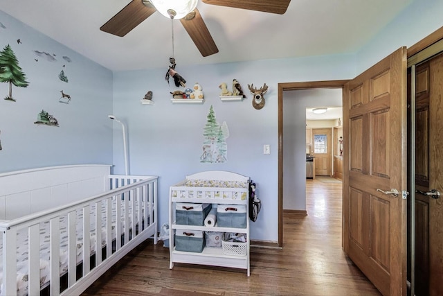 bedroom featuring wood finished floors, a crib, ceiling fan, and baseboards