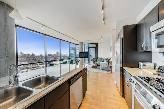 kitchen with appliances with stainless steel finishes, a sink, rail lighting, and light wood-type flooring