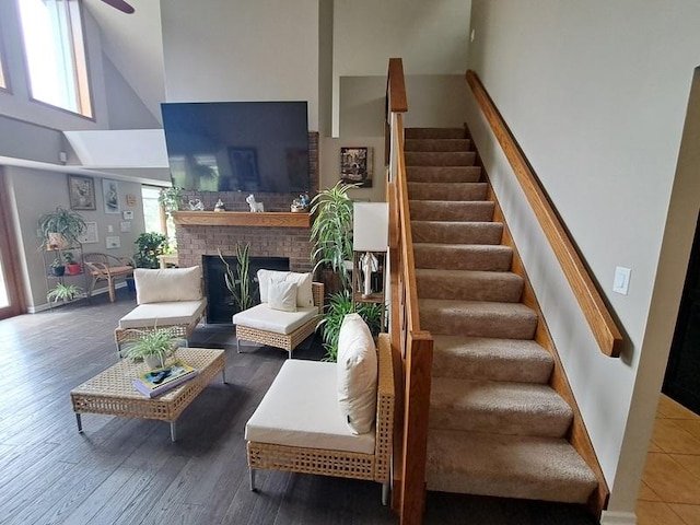 living room with a towering ceiling, stairs, wood finished floors, a ceiling fan, and a fireplace