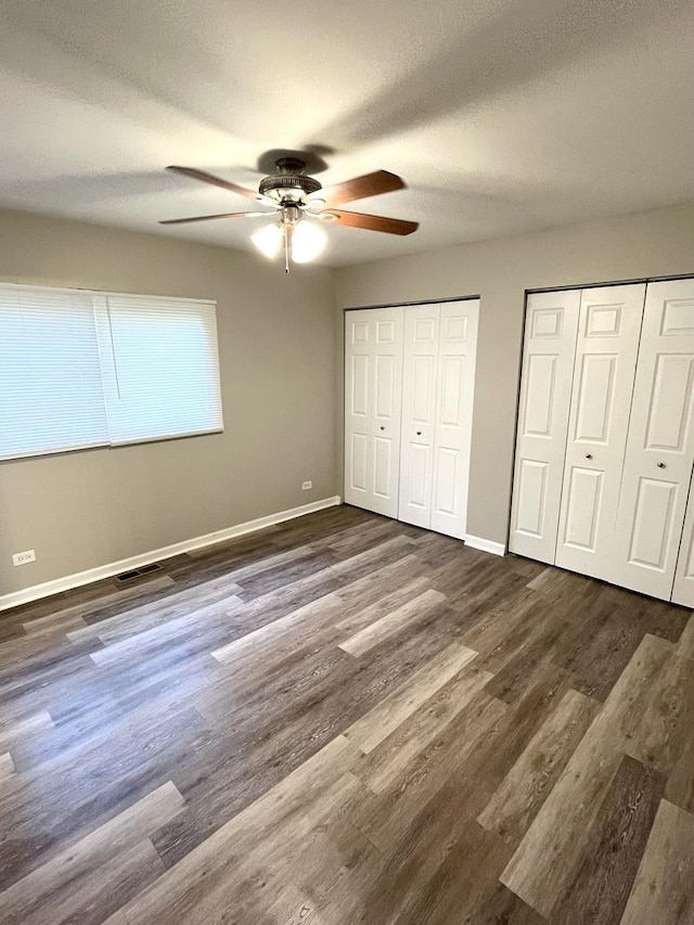 unfurnished bedroom featuring two closets, baseboards, dark wood-style flooring, and a ceiling fan