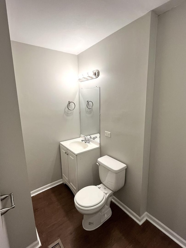 half bath with wood finished floors, vanity, toilet, and baseboards