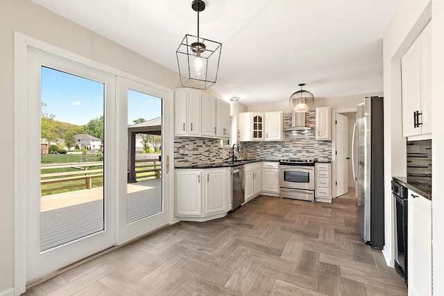 kitchen featuring appliances with stainless steel finishes, dark countertops, a sink, wall chimney exhaust hood, and tasteful backsplash