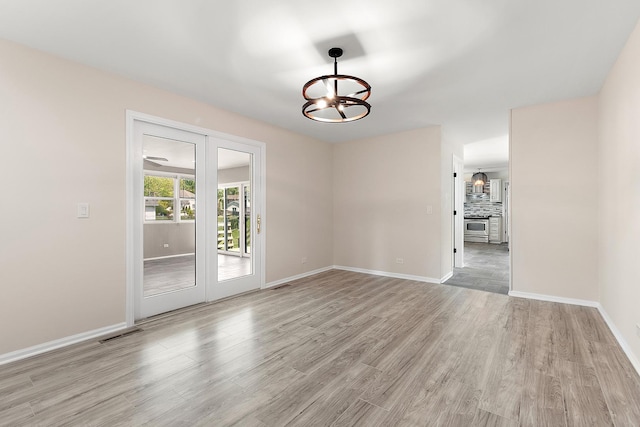unfurnished room with a chandelier, light wood-type flooring, and baseboards