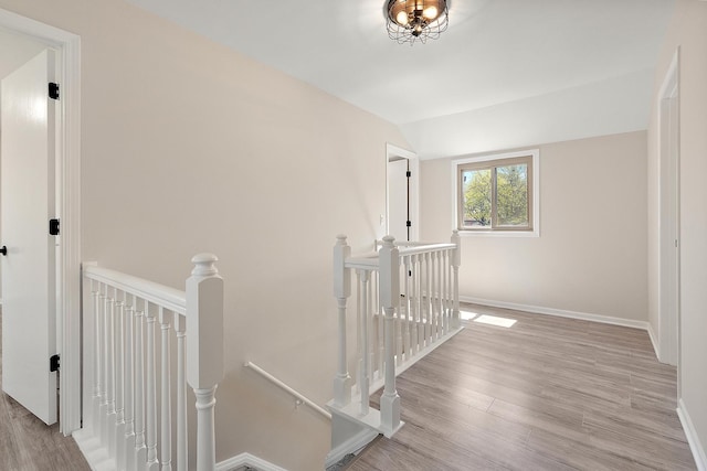 hall with an upstairs landing, vaulted ceiling, wood finished floors, and baseboards