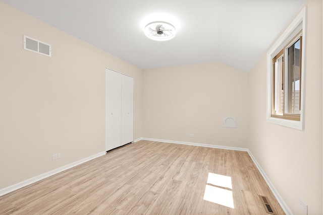 empty room with light wood-style floors, lofted ceiling, and baseboards