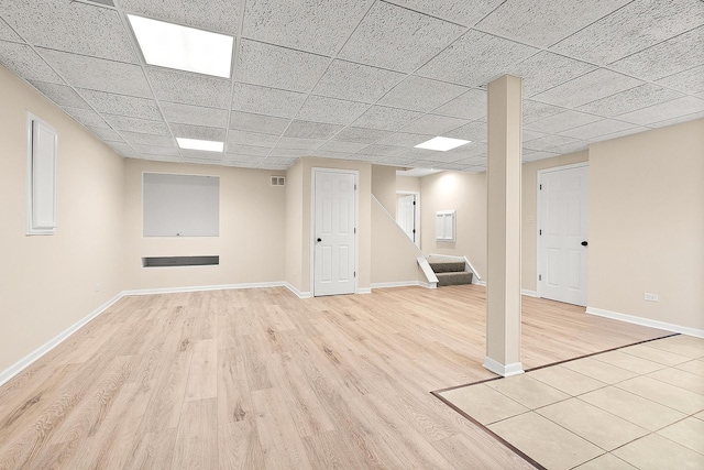 finished below grade area featuring stairway, light wood finished floors, baseboards, and a paneled ceiling